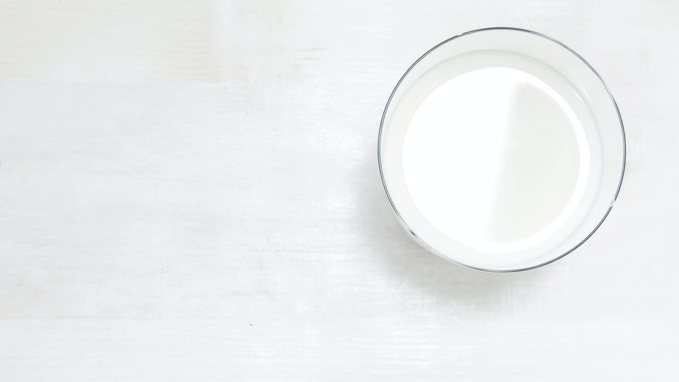 Photo from above of a glass of milk standing on a white table.