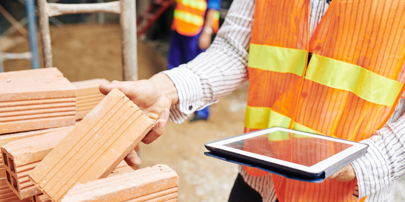 Close-up image of construction engineer reading list of building materials on digital tablet when checking pile of bricks