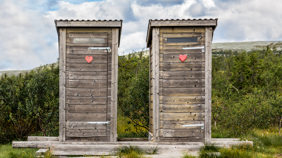Wooden outhouse toilets with red heart in mountain landscape.