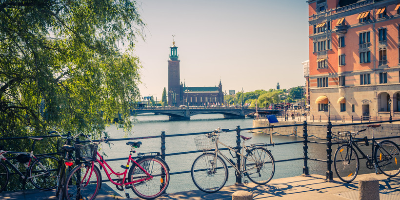 Bikes near bridge railing and Stockholm City Hall (Stadshuset) tower building of Municipal Council and venue of Nobel Prize on Kungsholmen Island, Lake Malaren water on sunny day with blue sky, Sweden