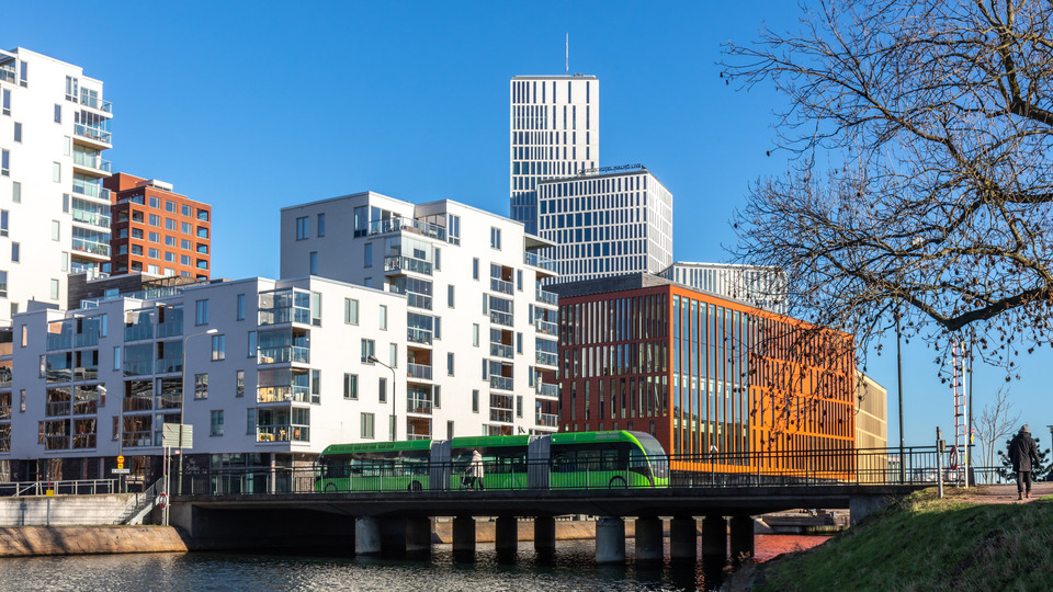 A green bus driving across a bridge over water, lots of tall building in back. Malmö Sweden 