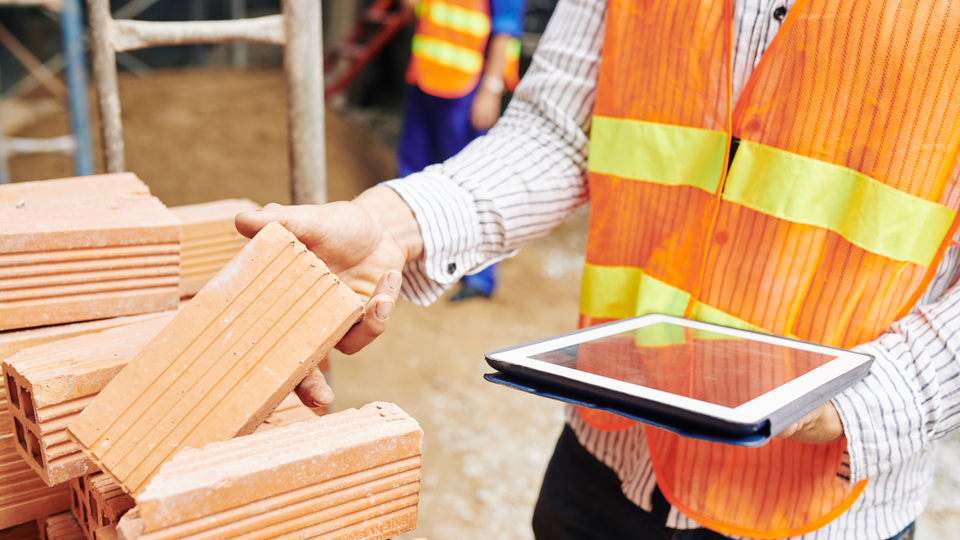 Close-up image of construction engineer reading list of building materials on digital tablet when checking pile of bricks